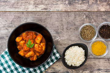 Chicken tikka masala with basmati rice in black bowl on wooden table
