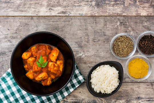 Chicken tikka masala with basmati rice in black bowl on wooden table

