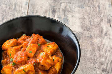 Chicken tikka masala in black bowl on wooden table

