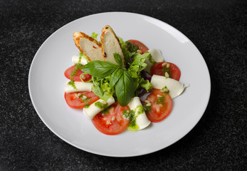 Salad with tomatoes basil and mozzarella with croutons on a white plate