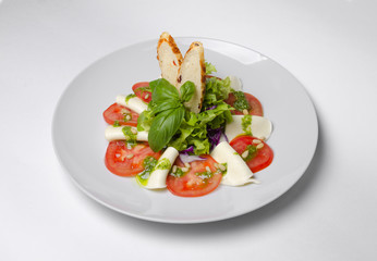 Salad with tomatoes basil and mozzarella with croutons on a white plate