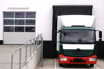 Lastkraftwagen an Laderampe  / Ein Lastwagen parkt an der Laderampe zum Beladen von Gütern und Materialien.