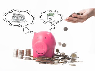 Woman Hand  putting coin into piggy bank for saving with pile of coins on white backgoound.A orange piggy bank are smile and happy .Many coin on the table.