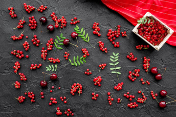 Berry theme. Red currant, cherry and leaves on black table background top view
