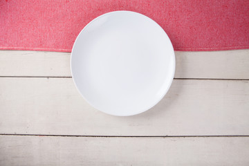 Top view of empty white plate put on red tablecloth and white wood table with space for copy.