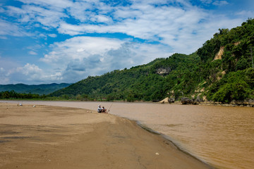 PACITAN BEACH, EAST JAVA, INDONESIA, FEB 21, 2016: Two unidentified person fishing at river estuary, brown sand, cloudy sky and green hills in background - Fishing is not just a hobby