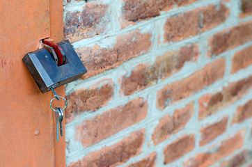 Padlock with key on metal door. Red brick wall