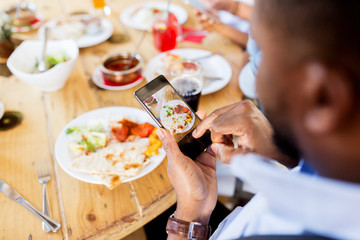hands with smartphone picturing food at restaurant