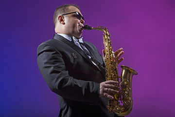 Fototapeta na wymiar Singer plays the saxophone. Man. European. He plays the saxophone. Dressed in a suit.