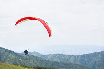 Paragliding in the sky. Paraglider flying over a mountain valley in summer sunny day.