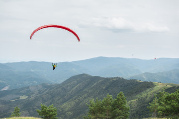Paragliding in the sky. Paraglider flying over a mountain valley in summer sunny day.