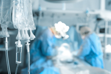 Intravenous system on the background of operating surgeons