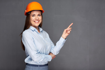 Woman wearing builder helmet pointing finger at copy space background.