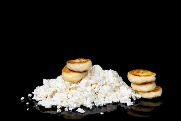 Heap of cottage cheese and delicious cheese cakes made out of it isolated on a black background