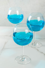Alcohol drink. Glasses with trendy blue wine, on white marble table background. Copy space