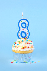 Iced birthday cupcake with with lit number 8 candle and sprinkles