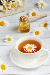 A Cup of chamomile tea and honey on white wooden background
