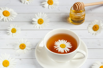 A Cup of chamomile tea and honey on white wooden background