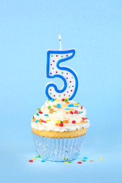 Iced birthday cupcake with with lit number 5 candle and sprinkles