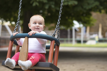 small active child happily swings on a swing in a summer park