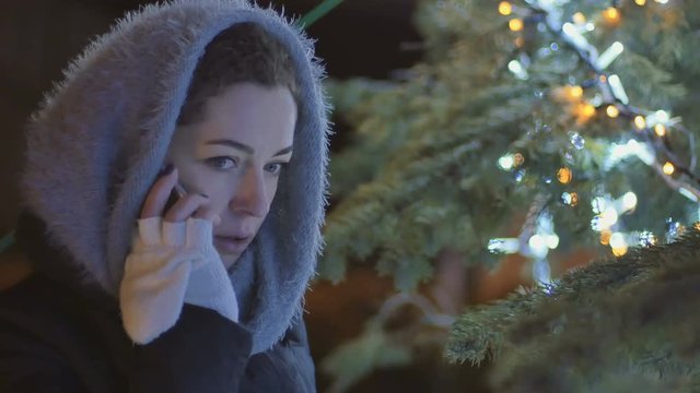 Young woman in scarf talks on phone at the fir-tree background