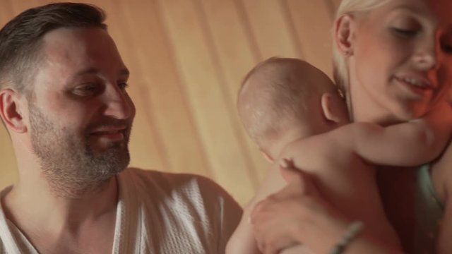 Family of four is basking in a wooden sauna. Young parents with two sons in the thermal zone bask in the sauna. A young married couple with two children in a sauna have a good time together.