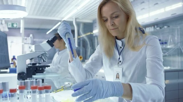 Female Medical Reasercher Works with Micropipette. She Tests Analysis. Scientists are Working in this Big Light Laboratory Shot on RED EPIC-W 8K Helium Cinema Camera.
