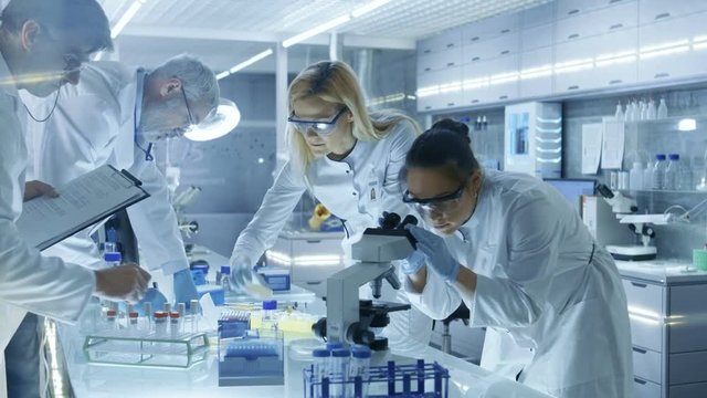 Team of Medical Research Scientists Work on a New Generation Disease Cure. They use Microscope, Test Tubes, Micropipette and Writing Down Analysis Results. Laboratory Looks Busy, Bright and Modern. 