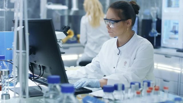 Medical Research Scientist Typing Information Obtained from New Experimental Drug Trial. She Works in a Bright and Modern Laboratory. Shot on RED EPIC-W 8K Helium Cinema Camera.
