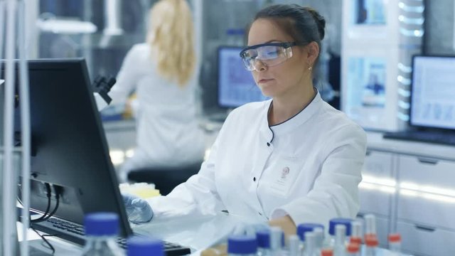 Medical Research Scientist Looks Into Petri Dish and Types on Her Personal Computer. She Works in a Modern Bright Laboratory. Shot on RED EPIC-W 8K Helium Cinema Camera.