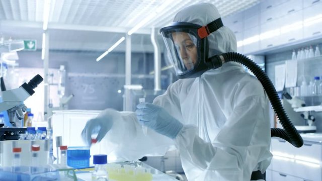 Medical Virology Research Scientist Works in a Hazmat Suit with Mask, She Takes out Test  Tubes from Refrigerator Box and Uses Micropipette. She Works in a Sterile High Tech Laboratory.