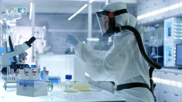 Medical Virology Research Scientist Works in a Hazmat Suit with Mask, She Takes out Test  Tubes from Refrigerator Box. She Works in a Sterile High Tech Laboratory.