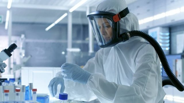 Medical Virology Research Scientist Works in a Hazmat Suit with Mask, She Uses Micropipette. She Works in a Sterile High Tech Laboratory, Research Facility. Shot on RED EPIC-W 8K Helium Cinema Camera.