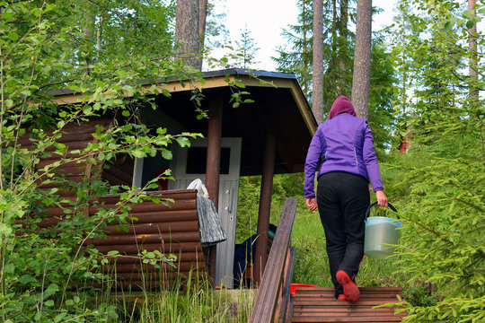 Woman Carrying Water From Lake To Barrel Shaped Sauna In Finland.