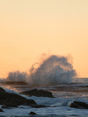 Splash of wave hitting rocks in golden hour light.