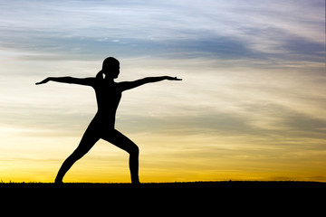 Silhouette of woman practicing warrior yoga at sunrise
