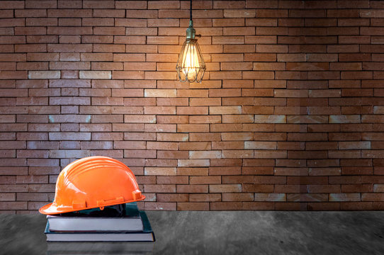 Education engineer concept.Orange helmet on book and background brick wall with bulb lights lamp