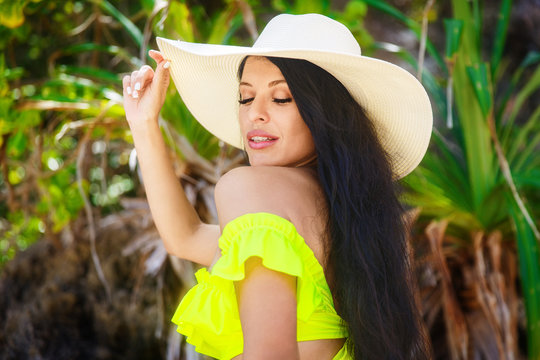 Beautiful brunette with long hair in bikini and straw hat on the jungle on a tropical beach. Summer vacation concept.