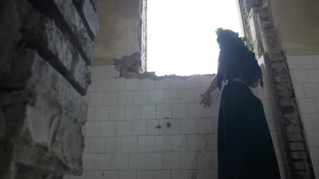 Scarred gothic woman entrapped in haunted building looking out the window and hiding from ghosts