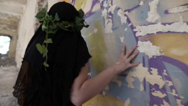Creepy gothic girl touching and listening the wall in a ruined room in search of ghosts