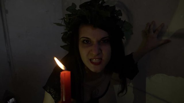 Exorcism of witch with evil sneer possessed by demon dressed in black snarling and holding a candle in her hand