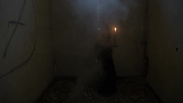 Gothic dressed vampire woman holding a candle turning around in a smoky abandoned house