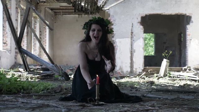 Witch woman in gothic clothes cursing during a ritual using a candle into a destroyed ruined building