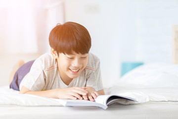 Happy Asian boy reading story book on the bed