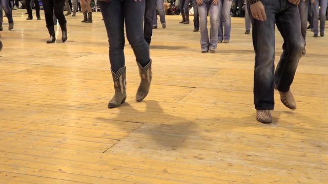 People dancing cowboy line dance at a folk country event, USA style. Legs moving together at American horse festival. Music tradition jeans boots and flag