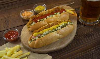Two hot dogs with French fries, spices and mug beer on a wooden table