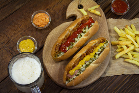 Two hot dogs with French fries, spices and mug beer on a wooden table