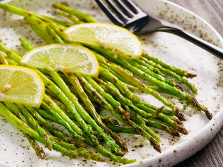 Close up view of grilled asparagus and slice of lemon in craft trendy plate on brown wooden table - Powered by Adobe