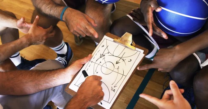 Upward view of coach assisting African American man players on clipboard clipboard