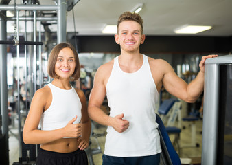 friendly young man and woman taking pause between exercising in gym
